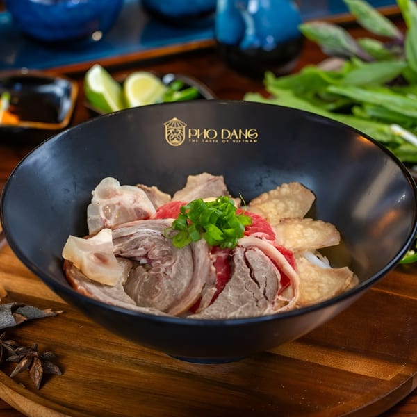 A black bowl of Pho Dang pho with various cuts of beef, garnished with green onions.