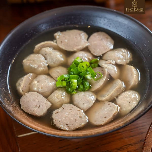 A close-up of a bowl of Pho Dang's Vietnamese meatball soup, garnished with chopped green onions.