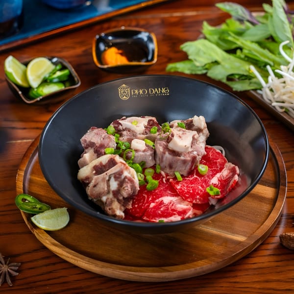 Pho Dang's pho with raw beef, oxtail, and green onions, surrounded by fresh herbs and lime.