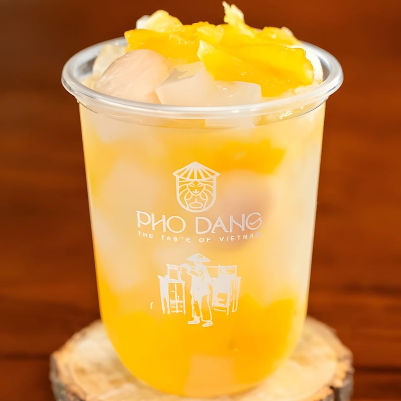 Pho Dang's mango and lychee drink with fruit chunks, on a wooden coaster.