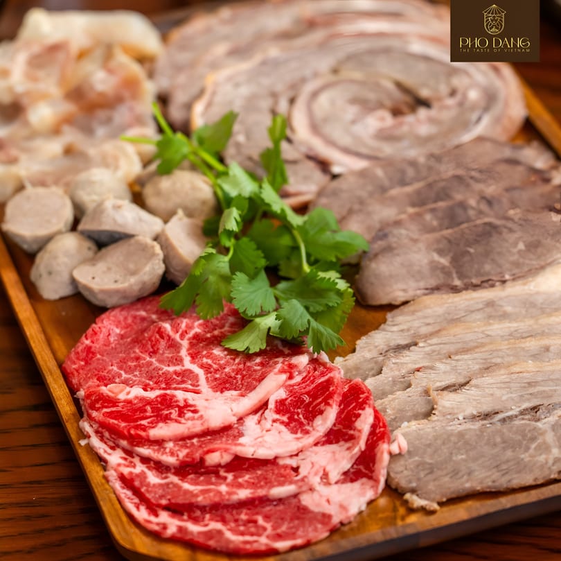 A wooden tray with various cuts of meat, meatballs, and cilantro for Pho Dang's hot pot.