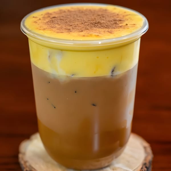 Iced coffee with a thick layer of yellow foam and a dusting of cocoa powder.