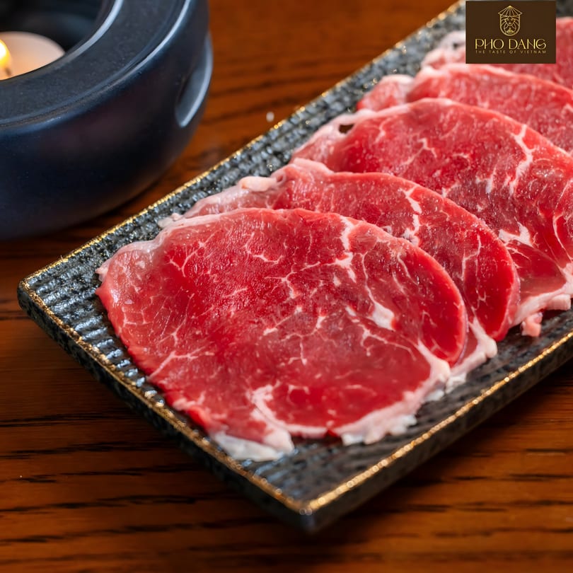Thinly sliced raw beef, likely for pho, arranged on a dark rectangular plate with a golden rim.